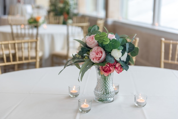 Closeup shot of a bouquet of elegant flowers in a glass vase surrounded by candles on the table