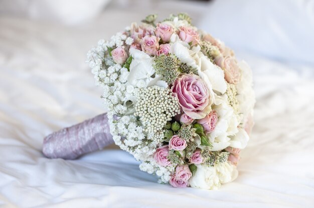 Closeup shot of a bridal bouquet on a white sheet with white, pink and green colors