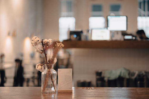 Closeup shot of a cafe wooden table with a jar of decorative flowers against a blurred background