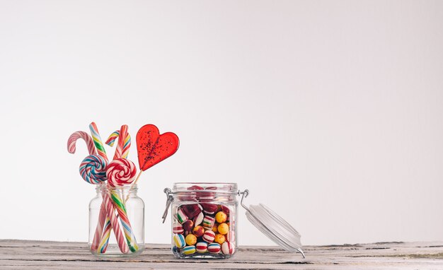 Closeup shot of candy canes and other candies in glass jars on a wooden surface