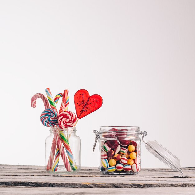 Closeup shot of candy canes and other candies in glass jars on a wooden surface