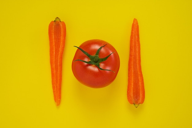 Closeup shot of carrots and tomato isolated on yellow.