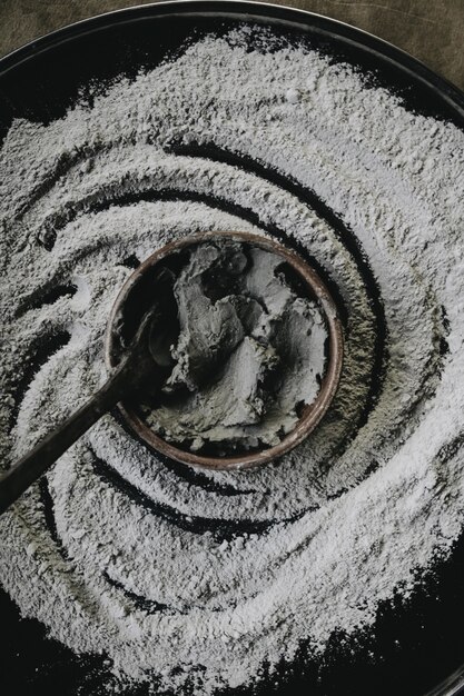 Closeup shot of a ceramic cooking pot with ingredients and a spoon in it with flour around