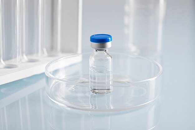 Closeup shot of a closed glass vial with clear liquid in a glass dish at a lab