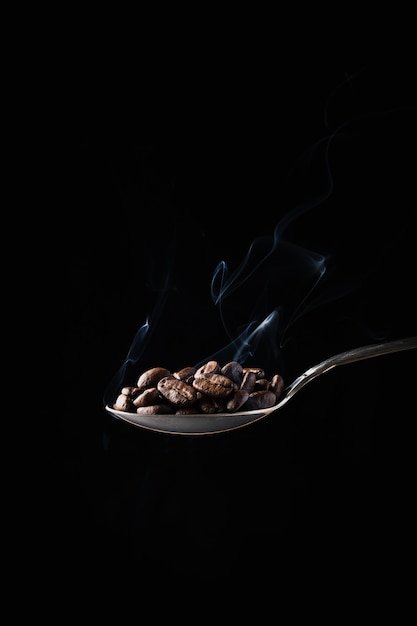 暗闇の中で煙をスプーンでコーヒー豆のクローズアップショット
