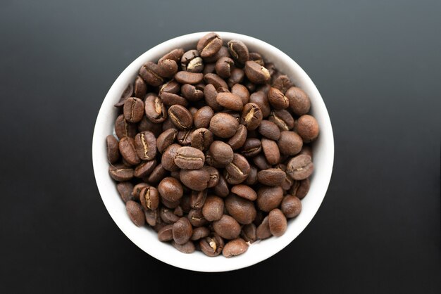 Closeup shot of coffee beans in a white bowl on a black wall