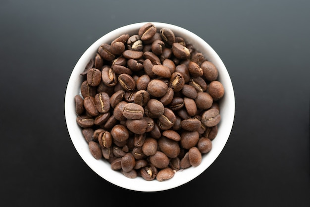 Closeup shot of coffee beans in a white bowl on a black wall