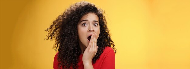 Closeup shot of concerned and shocked worried woman with curly hairstyle open mouth wide and coverin