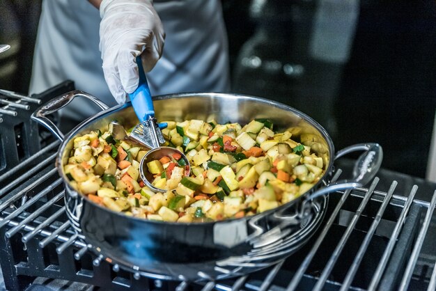 Крупным планом - повар готовит блюдо с овощами в металлической плите