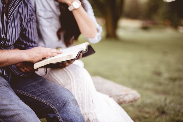 公園に座って、ぼやけた背景で聖書を読んでいるカップルのクローズアップショット