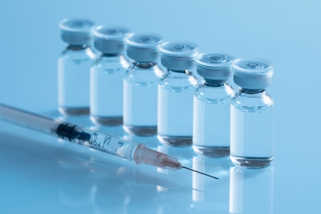 Closeup shot of covid19 vaccine bottles with a needle on a blue surface