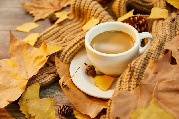 Closeup shot of a cup of coffee and autumn leaves on wooden background