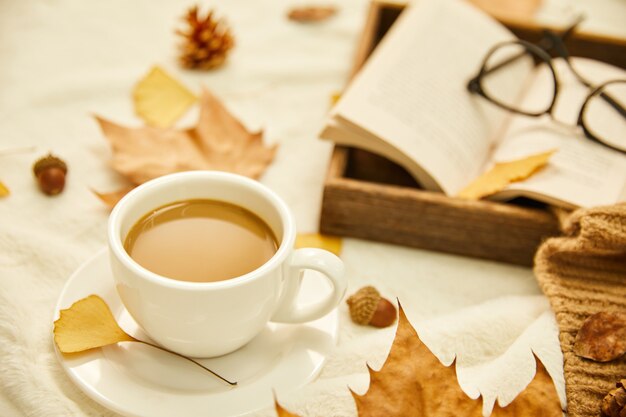 Closeup shot of a cup of coffee and autumn leaves on wooden surface