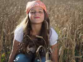 Free photo closeup shot of a cute little girl in a bandana sitting in the wheat field