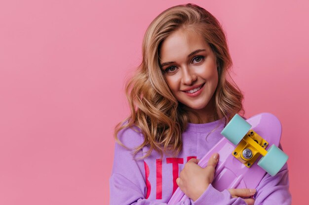 Closeup shot of debonair white woman with pretty smile Lovable girl holding skateboard on bright background