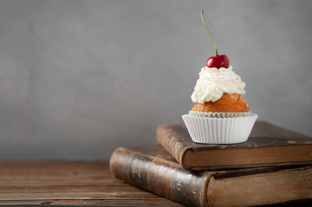 Снимок вкусного кекса со сливками и вишней сверху на книгах крупным планом