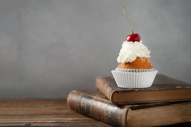 本の上にクリームとチェリーとおいしいカップケーキのクローズアップショット