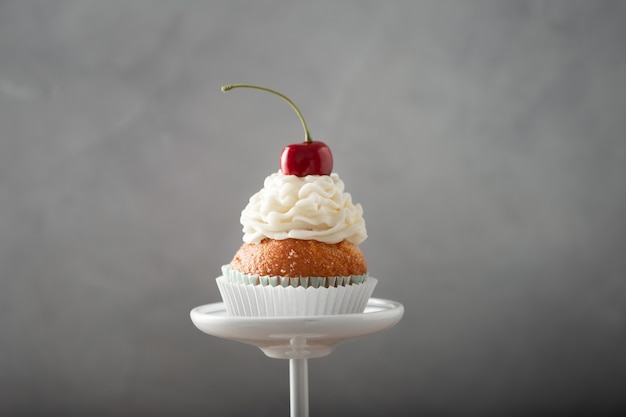 Closeup shot of a delicious cupcake with cream and cherry on top on a dessert stand