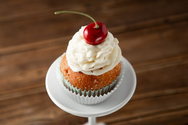 Closeup shot of a delicious cupcake with cream and cherry on top on a dessert stand