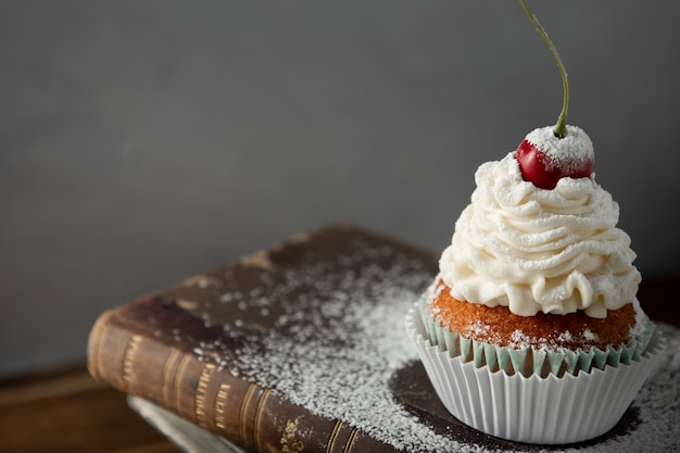 Closeup shot of a delicious cupcake with cream, powdered sugar, and a cherry on top on book