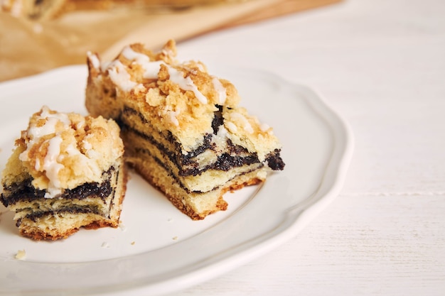 Closeup shot of delicious poppy seeds pieces of cake with a white sugar glaze on a white table