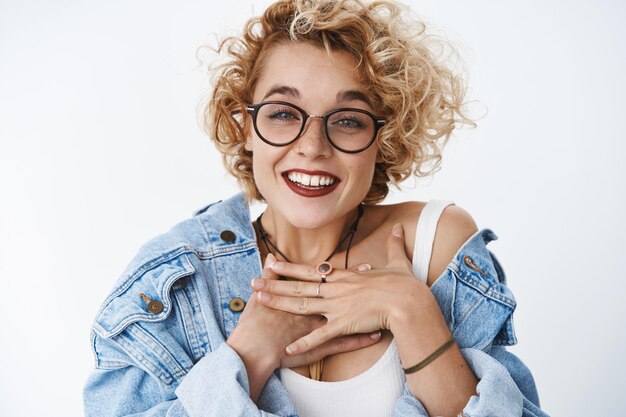 Free photo closeup shot of delighted and grateful impressed pretty charming woman with blond short curly haircut holding palms thankful on chest