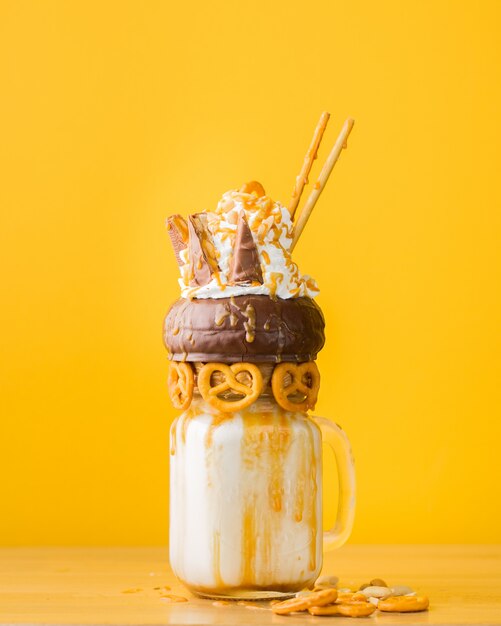 Closeup shot of a dessert with chocolate doughnut, whipped cream and salty pastry on a drinking jar