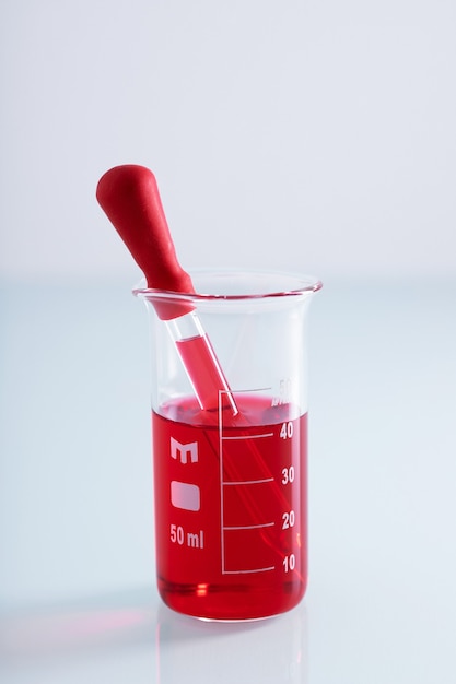 Closeup shot of a dropper in a beaker with red liquid on a white wall