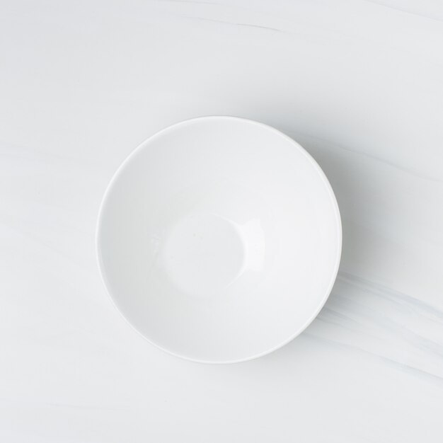 Closeup shot of an empty white ceramic bowl on a white wall