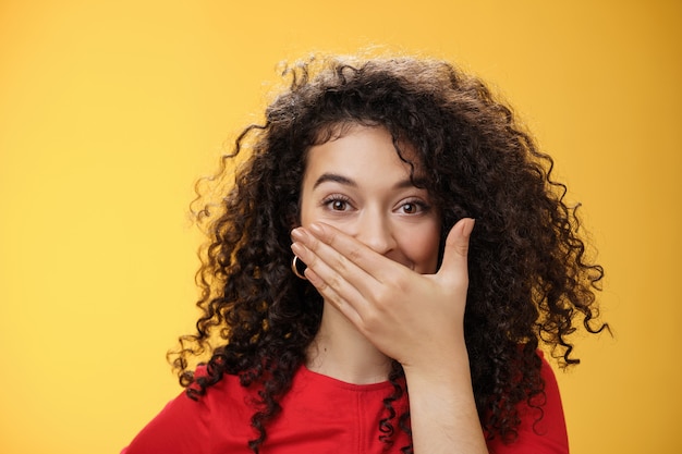 Closeup shot of excited and happy attractive female with curly hair giggling chuckling and covering ...