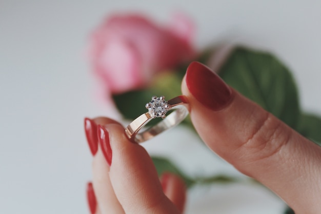 Крупным планом снимок женщины, держащей золотое бриллиантовое кольцо с розовой розой