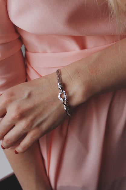 Foto gratuita colpo del primo piano di una donna in un abito rosa che indossa un bellissimo braccialetto d'argento con un ciondolo a cuore