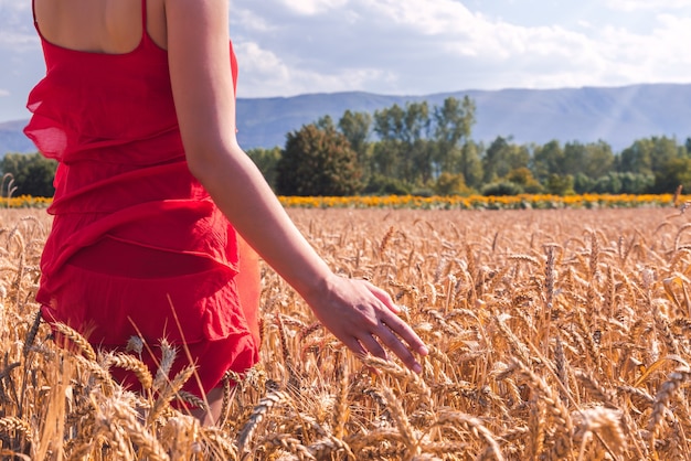 Foto gratuita primo piano di una donna con un vestito rosso in un campo di grano in una giornata di sole