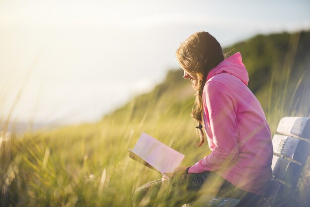 芝生のフィールドで聖書を読みながらベンチに座っている女性のクローズアップショット