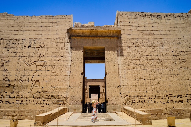 Closeup shot of a female standing in front of a Medinet Habu temple in Egypt