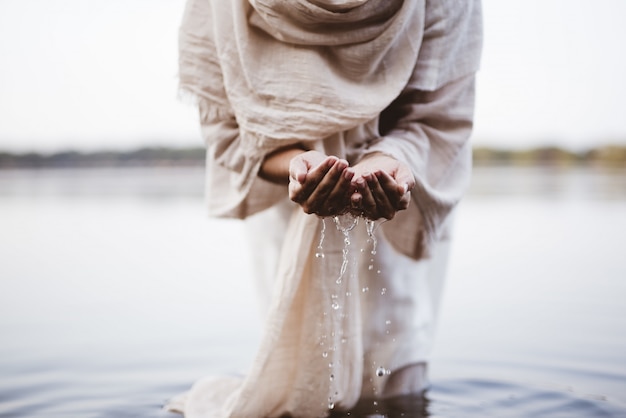 Foto gratuita il colpo del primo piano di una femmina che indossa un abito biblico che tiene l'acqua con le sue palme