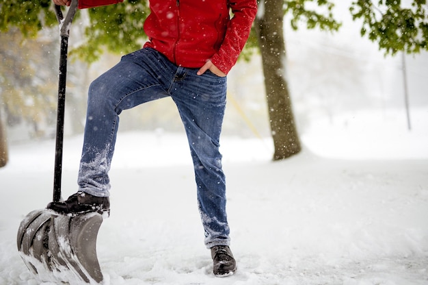 雪原に立っている間雪のシャベルに彼の足を持つ男性のクローズアップショット