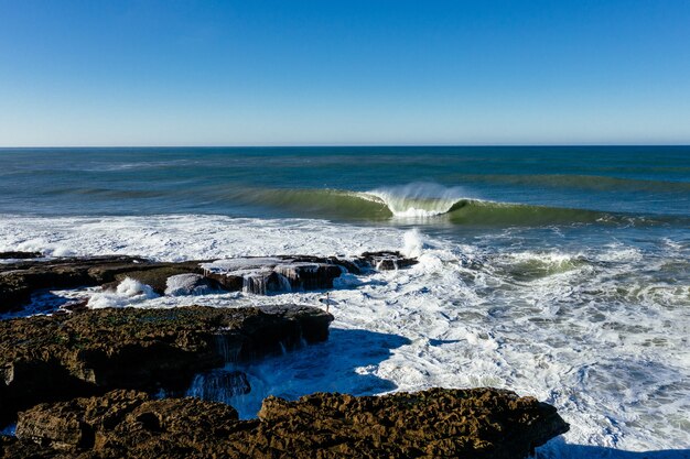 Closeup shot of foam waves hitting the rocky seashore on a sunny day