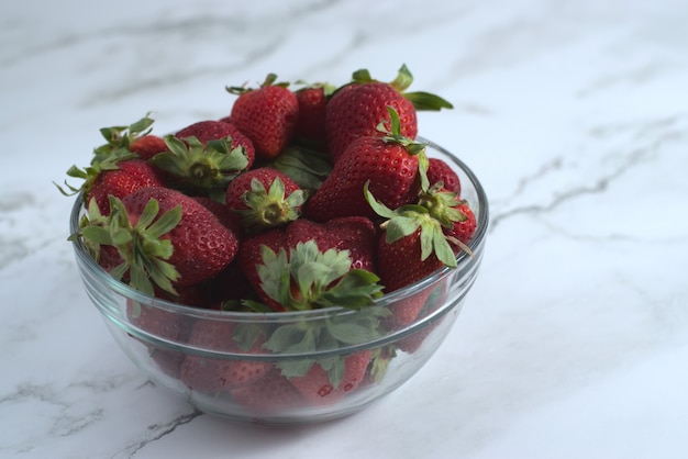 Closeup shot of fresh strawberries in a glass bowl on a ceramic surface