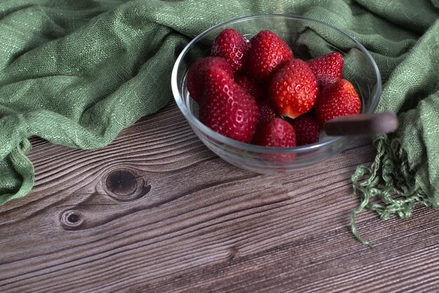 Closeup shot of fresh strawberries in a glass bowl and a green textile on a wooden surface