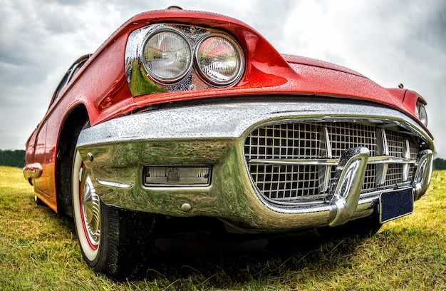 Foto gratuita colpo del primo piano della parte anteriore di un'auto rossa parcheggiata su un campo verde