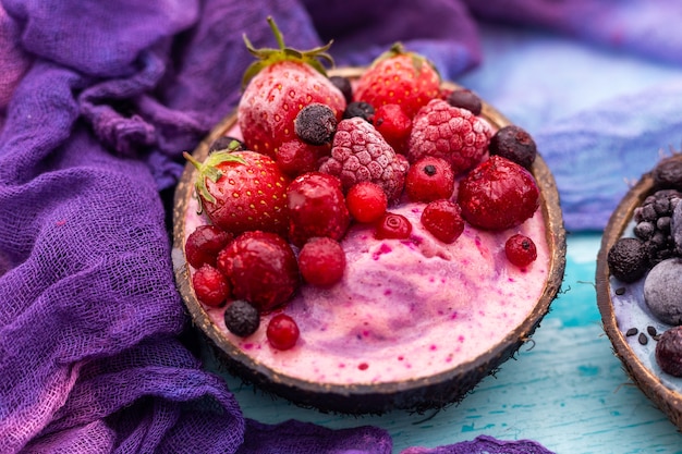 Closeup shot of a fruit shake topped with frozen strawberries, cranberries in a coconut bowl