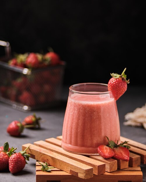 Closeup shot of a glass of fresh strawberry milkshake with strawberries on the table