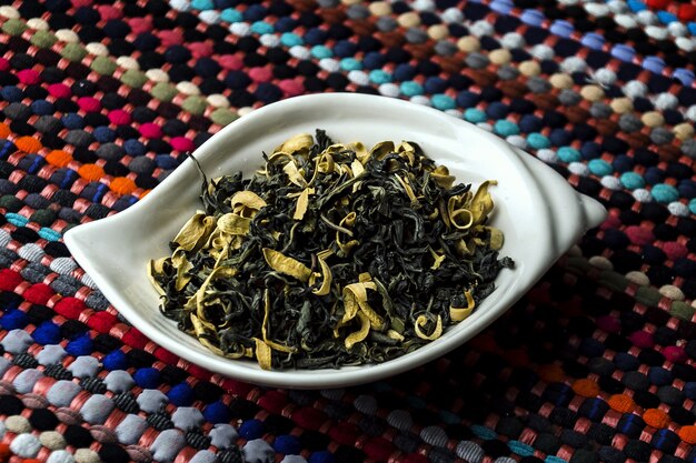 Closeup shot of green tea with orange blossom in a white plate on a colourful tablecloth