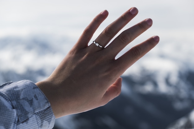 Closeup shot of a hand of a woman wearing a ring in front of the mountain