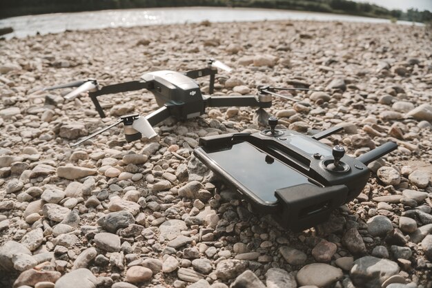 Closeup shot of a high-tech drone and its' remote control device on gray pebbles