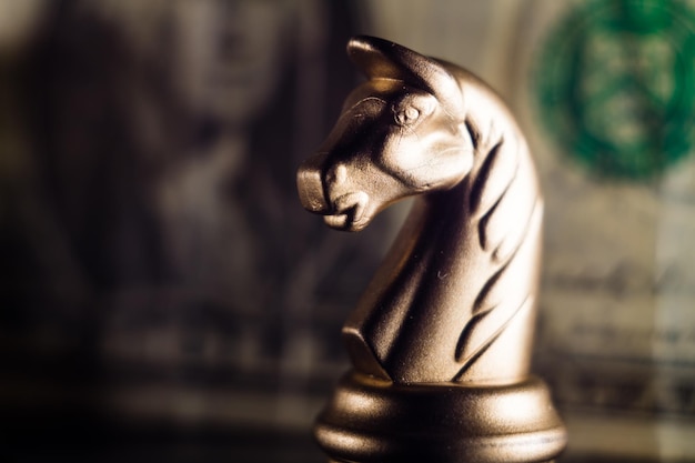 Free photo closeup shot of a knight on a chessboard with a dollar bill on a background