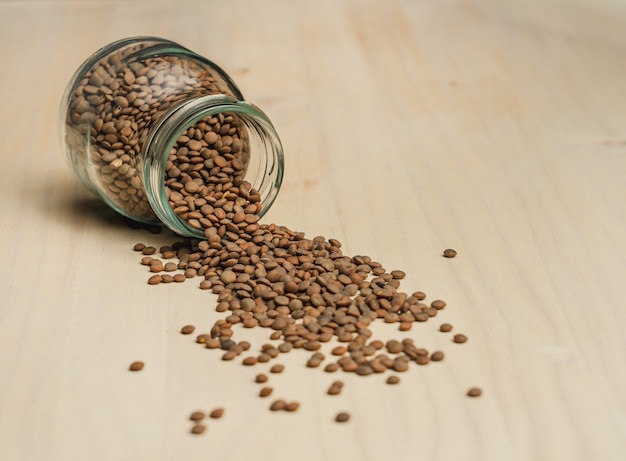 Free photo closeup shot of the lentils scattered on the wooden surface from the glass jar