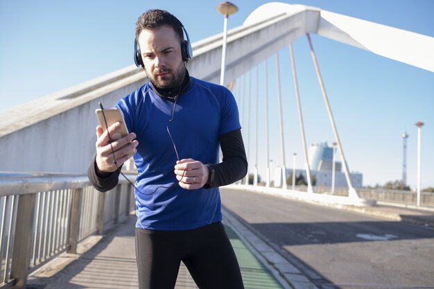 Крупным планом снимок мужчины в синих наушниках, использующего свой мобильный телефон во время пробежки по улице