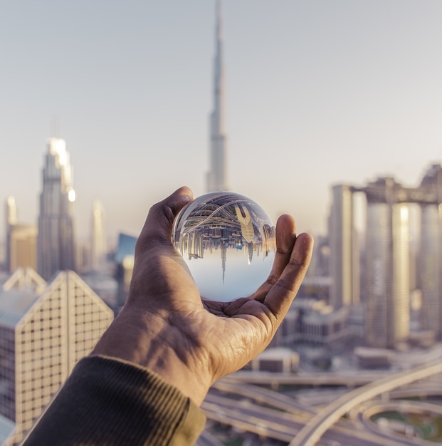 Free photo closeup shot of a male hand holding a crystal ball with the reflection of the city